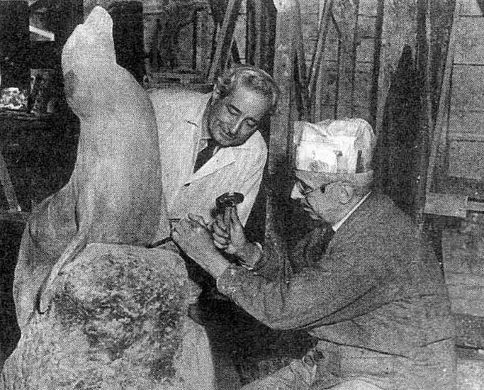 Sculptor with hammer in hand sculpting with assistant looking on